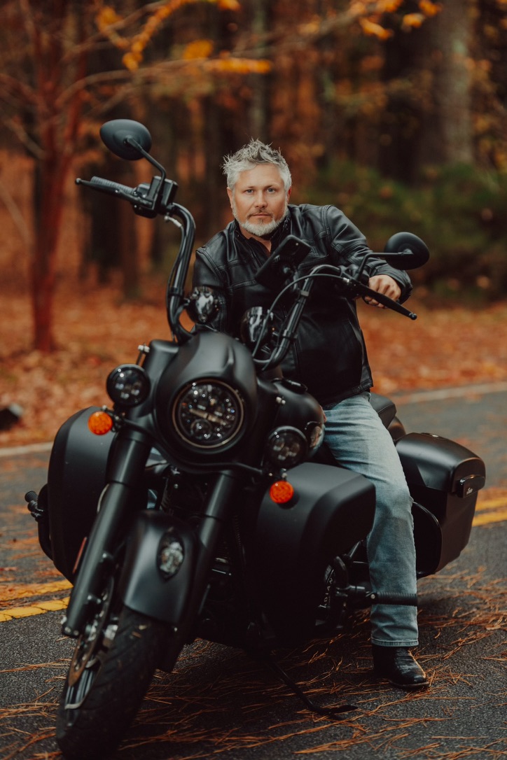Nicholas Davis seated on his motorcycle on a tree-lined road in autumn