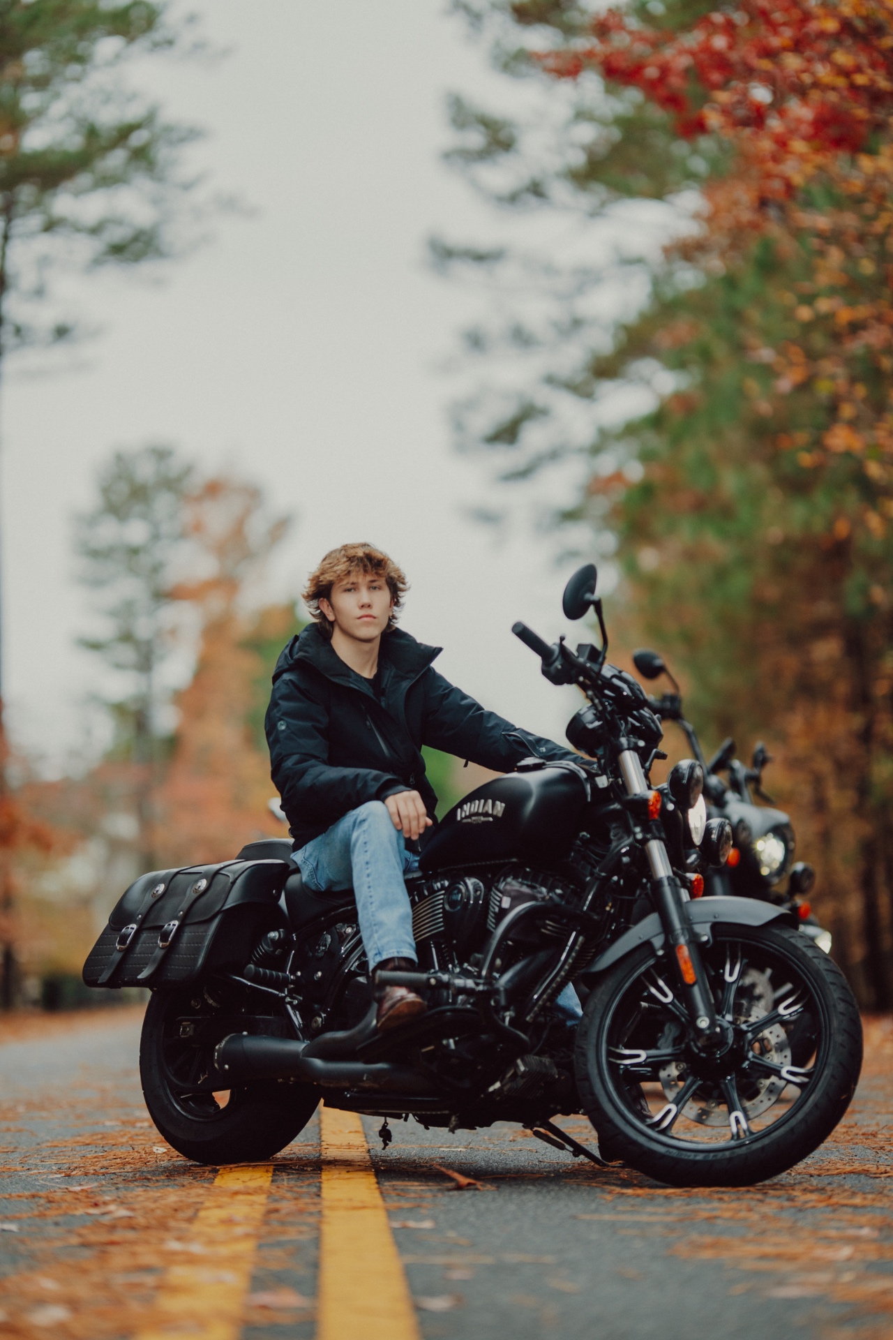Wyatt Davis seated on his black motorcycle on a tree-lined road in autumn